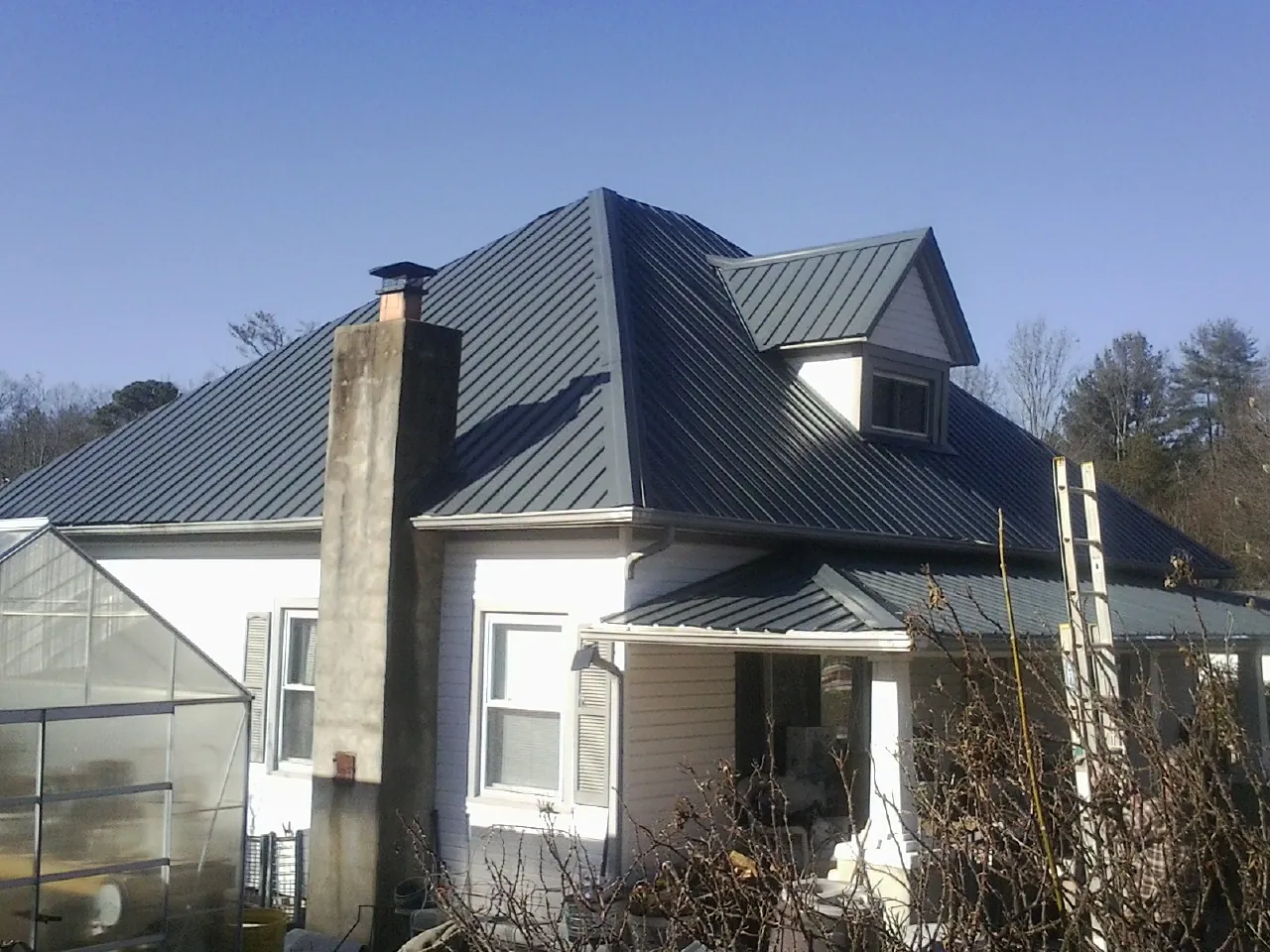Dark blue standing seam metal roof on a white farmhouse with dormer — Slate & Tile Roof Repair by Roofing Brothers in Harvard