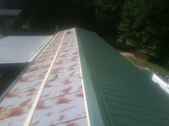 Old rusted panels beside newly installed green metal roofing in Harvard