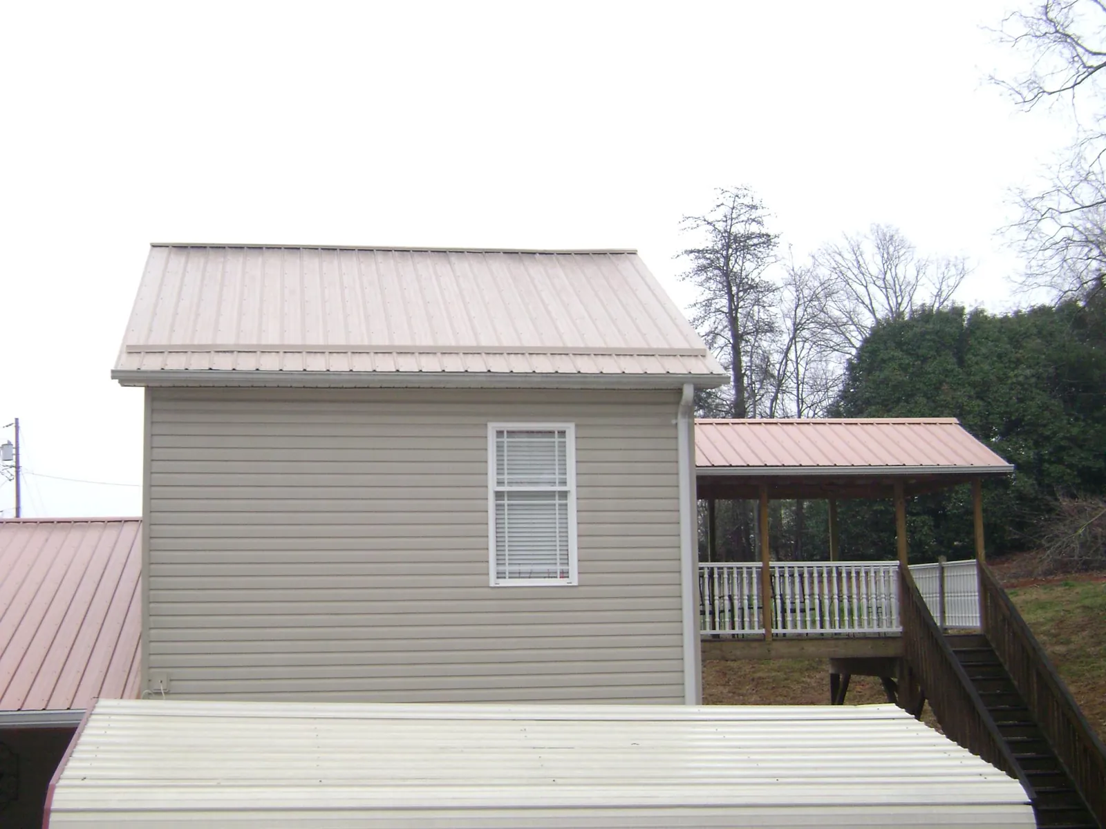 Tan metal roofs on a two story addition and attached porch, from a Roof Replacement job in Harvard